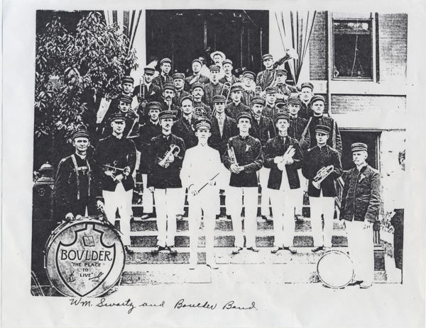 group of men wearing dark coats, white pants and dark caps, holding musical instruments. The bass drum head says 'Boulder the Place to Live' and there is a handwritten caption which reads, 'Wm. Swartz and Boulder Band.'