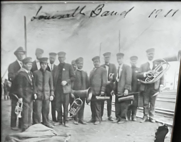 a small group of men holding musical instruments. 'Louisville Band 1911' is written across the top of the photo.
