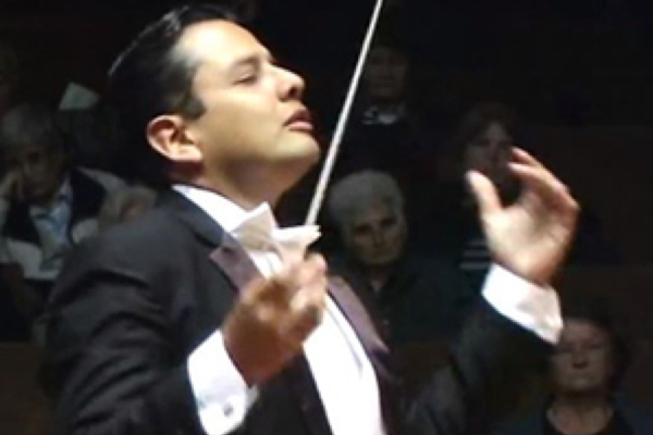 conductor in black tux with white shirt and bow tie, with baton raised