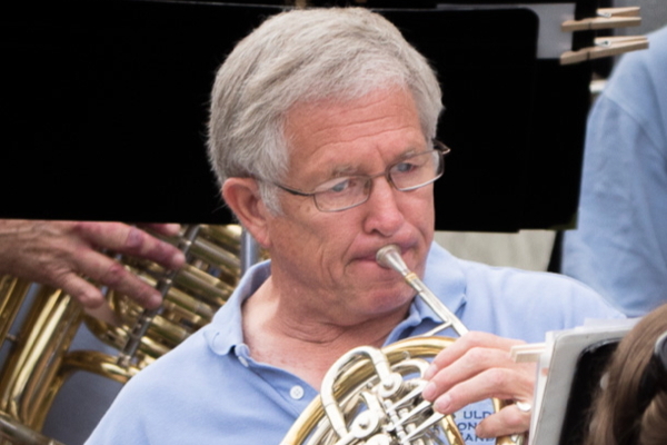man in light blue polo shirt playing french horn outdoors