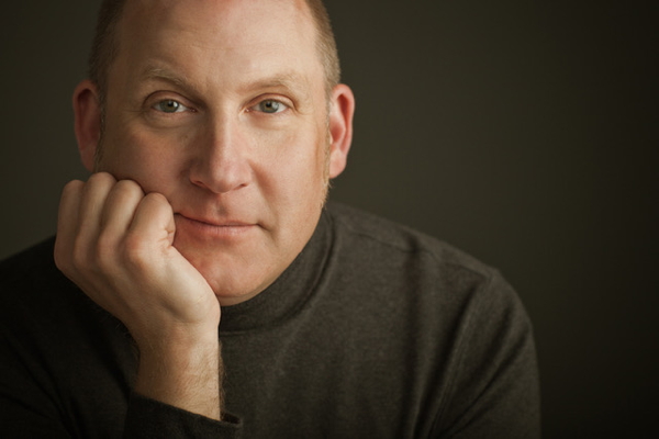 man wearing dark turtleneck, resting his chin in his hand