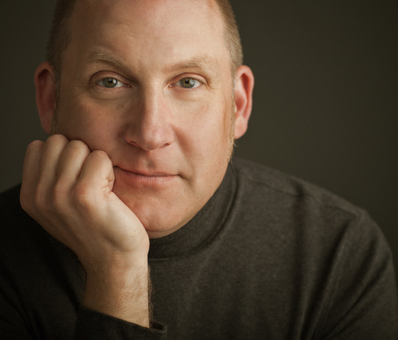 man wearing dark turtleneck, resting his chin in his hand