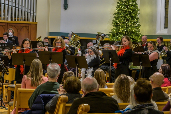 five flutists standing and playing in front of the band