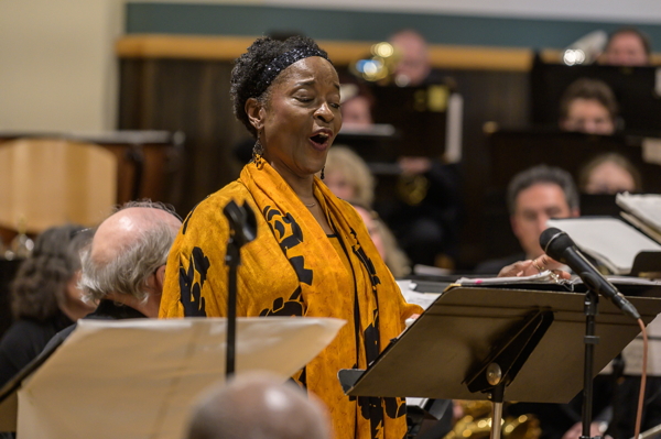 woman in yellow and black dress, singing in front of the band