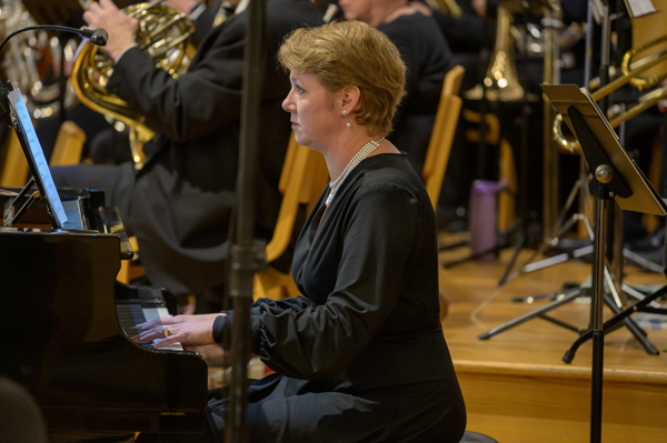 blonde woman in black dress seated at piano with band to her right