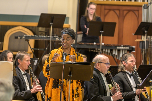 woman in yellow and black dress, singing in front of the band