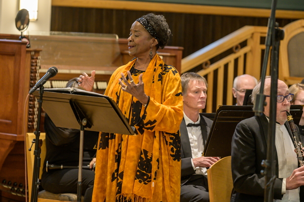 woman in yellow and black dress, singing in front of the band