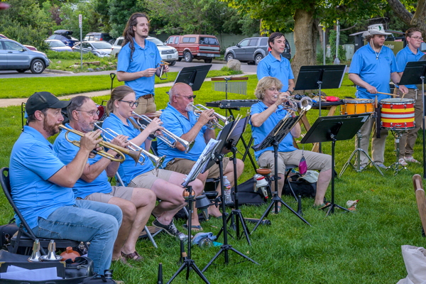 five trumpet players in blue shirts, seated in front of four percussionists