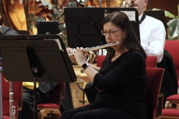 dark-haired woman wearing a black dress and glasses, playing a flute