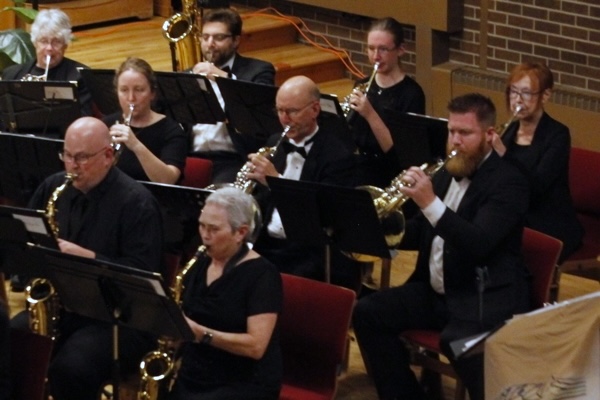 people dressed in black concert attire, playing saxophones and french horns