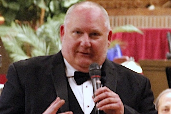 man in black suit, white shirt, black bow tie, holding a microphone