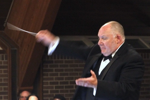 man in black suit, white shirt, black bow tie, waving a conductor's baton