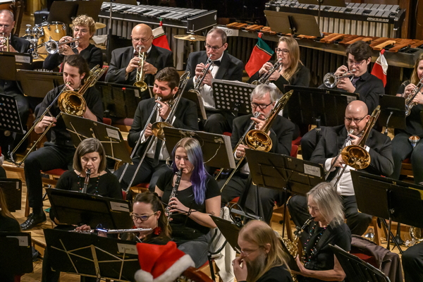 people seated in black concert attire, playing brass and woodwind instruments