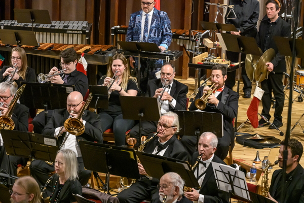 people seated and standing, playing brass and percussion instruments and saxophones