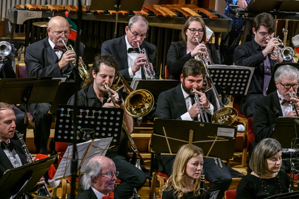 people seated, wearing black and white, playing trumpets and trombones