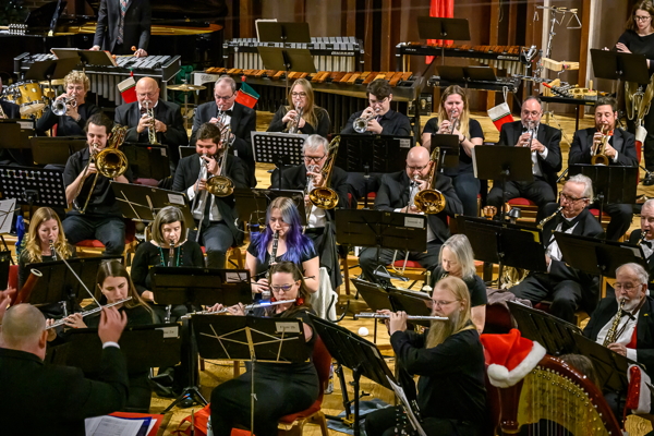 people playing trumpets, trombones, flutes and saxophones, facing a man in black suit