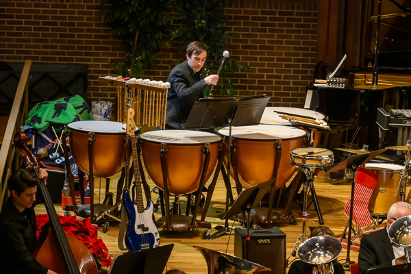 man in black shirt, playing four timpani, witha  string bass player to the left