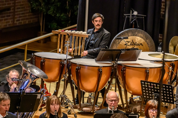 man in mustache, wearing all black, playing four timpani. A Zildjian gong hangs behind him.
