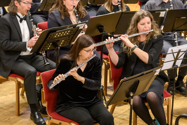 two women playing flutes, seated in front of two people playing clarinets