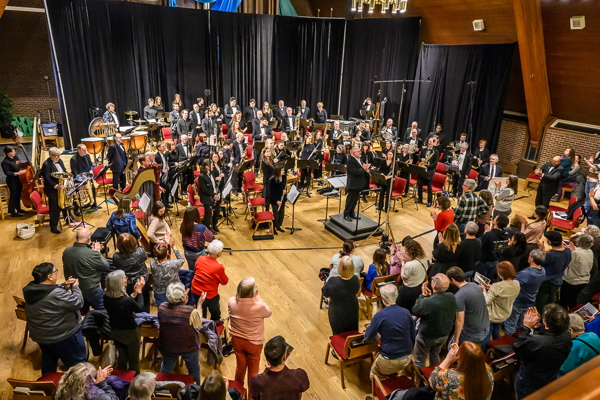 a concert band standing after performing, receiving a standing ovation from the audience