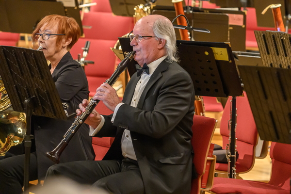 red-haired woman and a man, both wearing glasses. The woman plays french horn, and the man plays clarinet