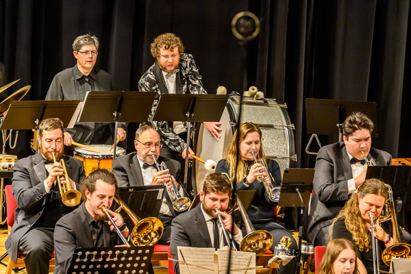 trumpet and trombone players seated in front of two percussionists