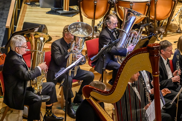 side view of three men playing tubas, with a large harp in front of them