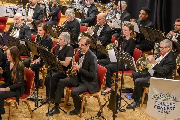 side view of a group of musicians dressed in black, playing saxophones and french horns