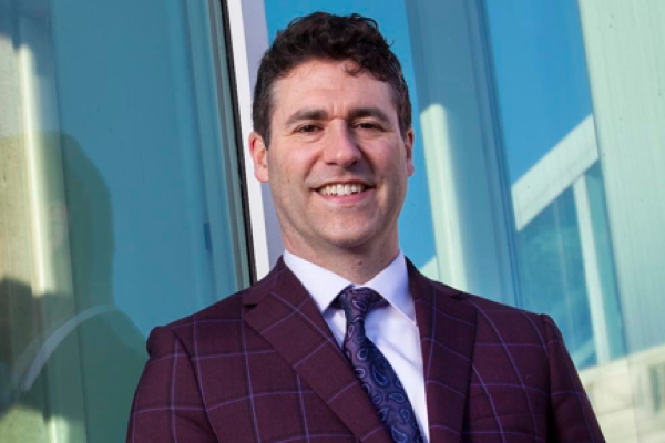 smiling man with dark hair in purple suit jacket and purple tie