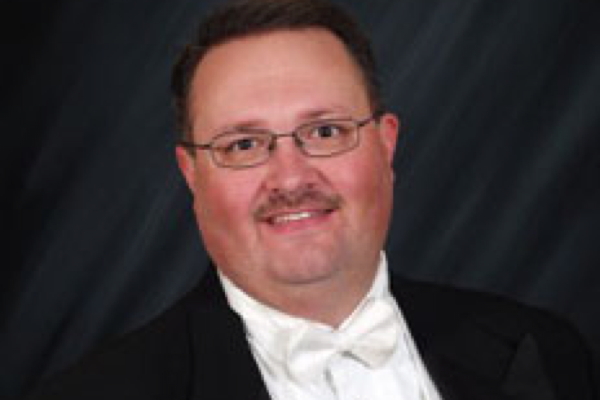 smiling man with wire glasses, wearing black tux, white shirt and white bow tie