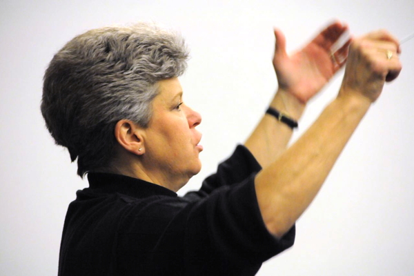 woman with short hair, black top, with hands raised to conduct